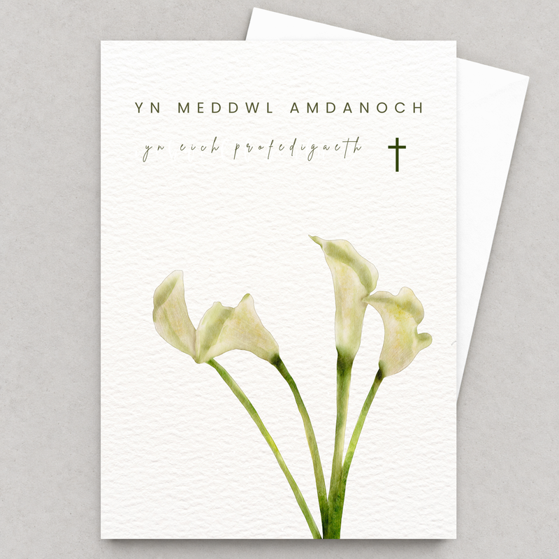 Cerdyn cydymdeimlad gyda lilïau gwyn a chroes fach, yn gorwedd yn fflat gydag amlen wen
