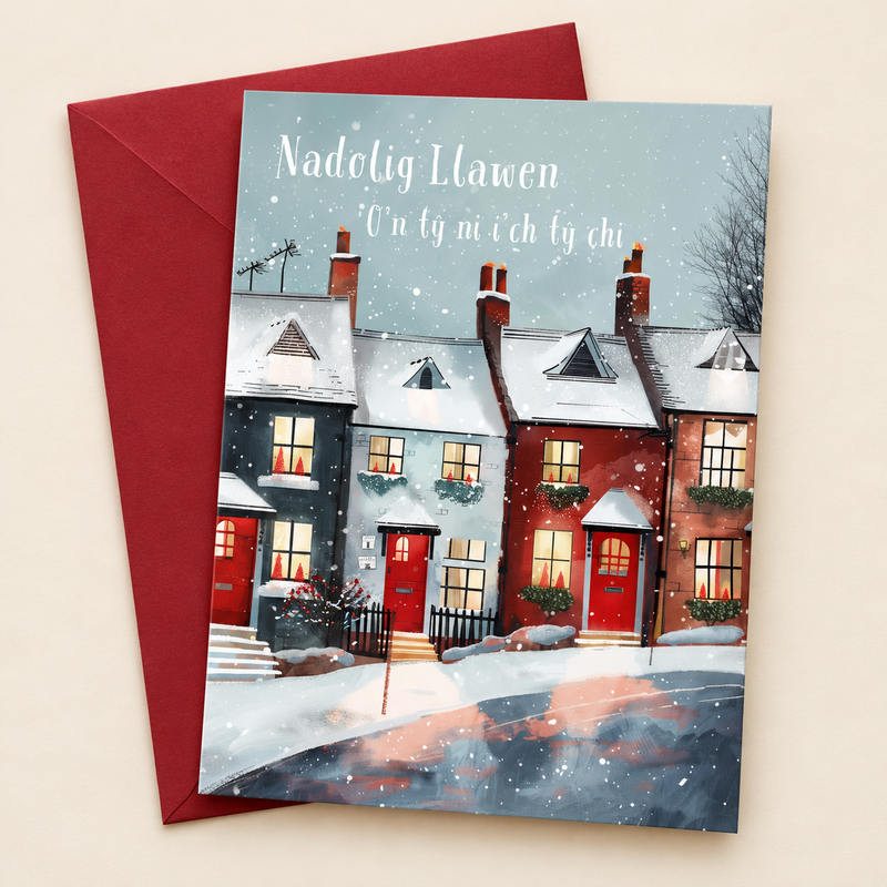 Cerdyn Nadolig O’n Tŷ Ni i’ch Tŷ Chi – Tai / Welsh Christmas card with a row of houses in the snow, lying flat beside a deep red envelope.