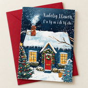 Cerdyn Nadolig O’n Tŷ Ni i’ch Tŷ Chi – Eira / Welsh Christmas card with a blue cottage in the snow, lying flat beside a deep red envelope.
