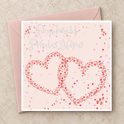 Cerdyn Penblwydd Priodas Hapus gyda dwy galon binc gydgysylltiedig, yn wastad gydag amlen binc / Welsh anniversary card shown flat with a pink envelope.