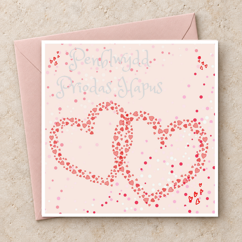 Cerdyn Penblwydd Priodas Hapus gyda dwy galon binc gydgysylltiedig, yn wastad gydag amlen binc / Welsh anniversary card shown flat with a pink envelope.