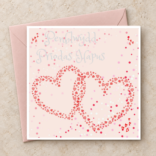 Cerdyn Penblwydd Priodas Hapus gyda dwy galon binc gydgysylltiedig, yn wastad gydag amlen binc / Welsh anniversary card shown flat with a pink envelope.